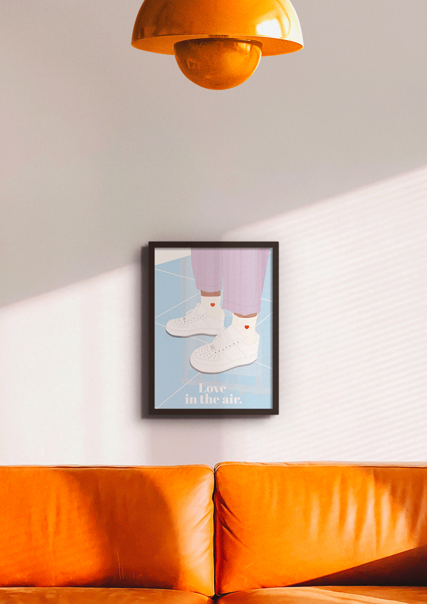 Affiche Love in the air encadrée noir, accrochée au-dessus d'un canapé orange